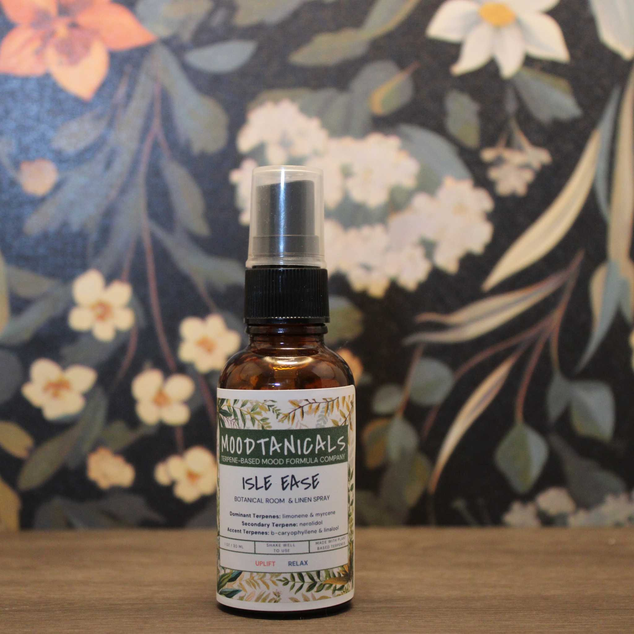 Moodtanicals Isle Ease spray bottle on a wooden surface with a floral background