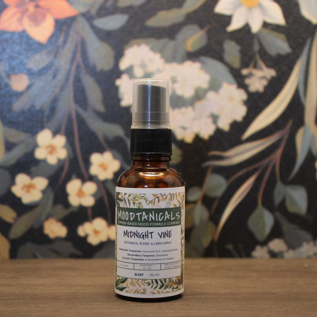 Bottle of Moodtanicals Midnight Vine spray on a wooden surface with a floral background