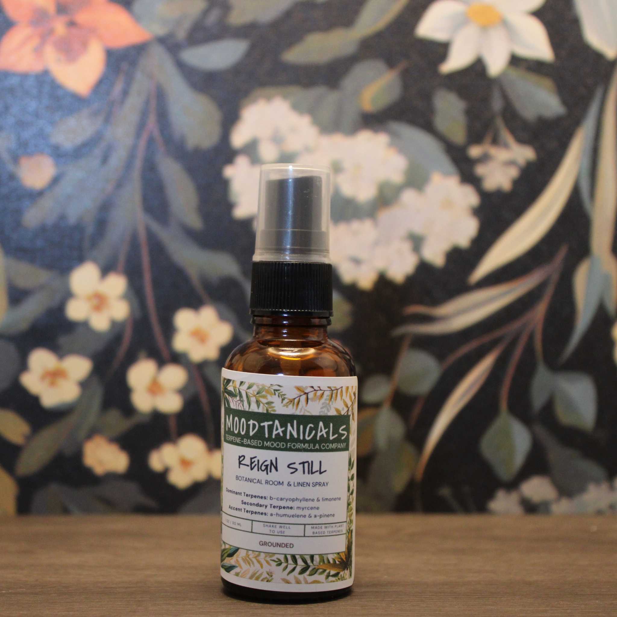 Bottle of Moodtanicals Reign Still spray with a floral background