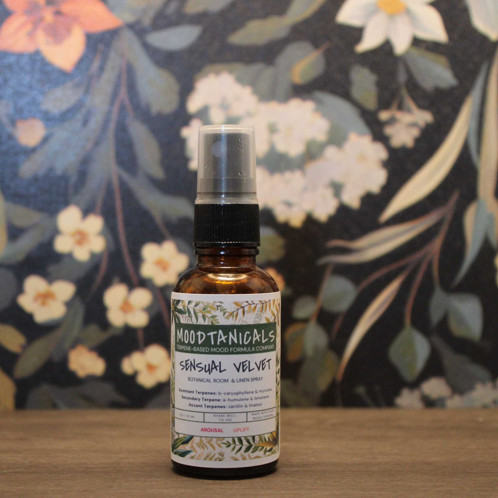 Bottle of Moodtanicals Sensual Velvet product on a wooden surface with a floral-patterned background