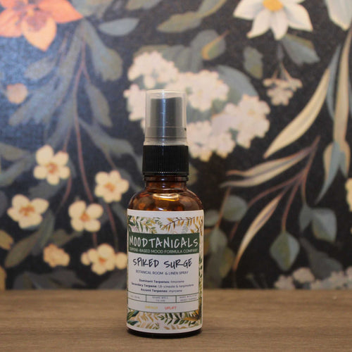 Bottle of 'Moodtanicals Spiced Surge' on a wooden surface with a floral background