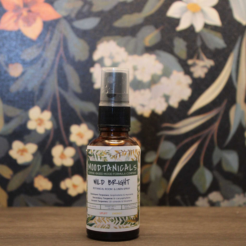 Bottle of Moodtanicals Wild Bight room spray on a wooden surface with a floral background